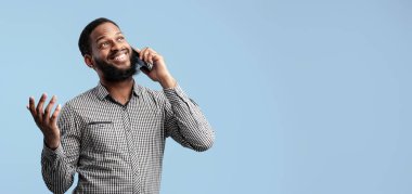 Modern İletişim Konsepti. Gülümseyen Afro-Amerikan Sakallı Adam cep telefonuyla konuşuyor Mavi Stüdyo 'nun arkasında tek başına duruyor. Neşeli siyahi adam telefon etmek için Gadget kullanıyor.