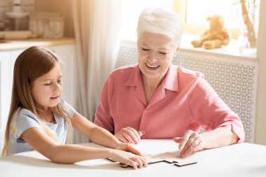 Aile hobileri. Yaşlı kadın ve torunu mutfakta bulmaca oynuyorlar.
