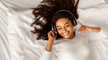 Yüksek açılı, tatmin olmuş, kablosuz kulaklık takmış, evde beyaz çarşafların üzerinde uzanmış, müzik dinleyen, afiş, bedava fotokopi alanı...