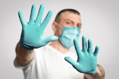 Sosyal Mesafe. Tıbbi Maskeli Adam Coronavirus salgını sırasında elleri gri arkaplanda durarak hareket etmeyi bırakıyor. Panorama, Seçici Odaklanma