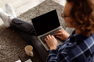 Evdeki katta oturan adamın boş ekranlı dizüstü bilgisayarı kullanışının arka görüntüsü. Adam bilgisayarda interneti tarıyor. Çevrimiçi Teknoloji, Uzak Çalışma Konsepti. Mockup, Yüksek Açı Çekim