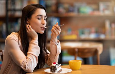 Mutlu Arap bayan tatlıyı ve kahveyi kapalı gözlerle yiyor, kafede oturuyor. Pasta yiyen ve sıcak içecek içen genç bir kadın, işte mola veren, kafeteryada vakit geçiren, boş alan