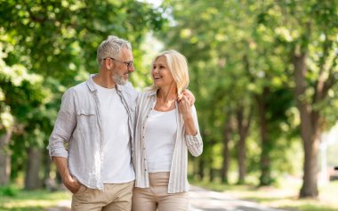 Romantik son sınıf çifti yaz parkında yürüyor ve mutlu olgun eşleri kucaklıyor, kucaklıyor ve birbirlerine gülümsüyor, neşeli karı-koca dışarıda yürüyüşten keyif alıyor, Uzay 'ı kopyalıyor.