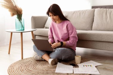 İçişleri Bakanlığı Konsepti. Bilgisayarla çalışan ve klavyede daktilo kullanan odaklanmış genç bayan yöneticinin portresi. Finansal rapor yazmakla meşgul bir kadın, yere oturmuş, kanepeye yaslanmış.