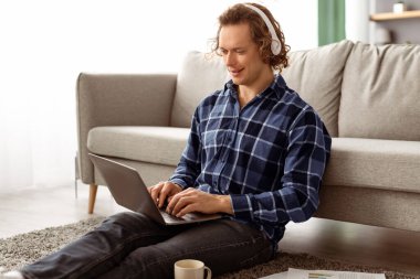 Kulaklıklı gülen adam dizüstü bilgisayar kullanıyor video görüşmesi yapıyor ya da evde oturmuş internette çalışıyor. Uzak Görev ve Modern İletişim, İnternet ve Teknoloji Konsepti