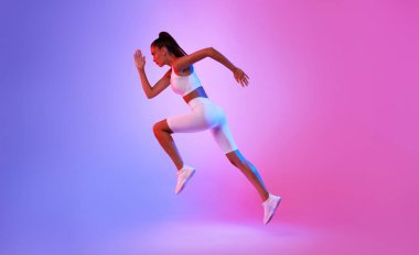 Pembe ve Mavi Neon Stüdyosu 'nun arka planında, beyaz spor giysiler içinde, kardiyo antrenmanı sırasında orta havada koşan kararlı sporcu kadın. Fitness ve Spor Konsepti. Yan Görünüm, Tam Uzunluk