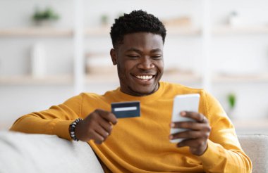 Evde cep telefonu ve kredi kartı kullanan, internet üzerinden mal ve hizmetleri ödeyen, finansal mobil uygulama kullanan, fotokopi çeken genç bir adam. E-ticaret, online alışveriş konsepti