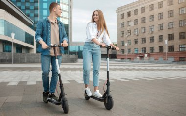 Hadi biraz eğlenelim. Kaygısız bir çiftin motorlu scooter sürerken, eğlenirken ve birlikte vakit geçirirken tüm vücut boyu fotoğrafı. Pozitif erkek ve kadın rahatlıyor, birbirlerine bakıyorlar.