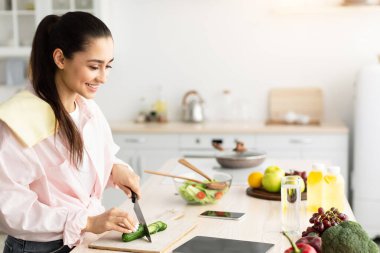 Dijital tablete bakan genç bayanın portresi yeni yemek tarifleri deneyen, modern mutfaktaki dairesinde duran. Kilo Verme ve Sağlıklı Beslenme Web Sitesi Konsepti