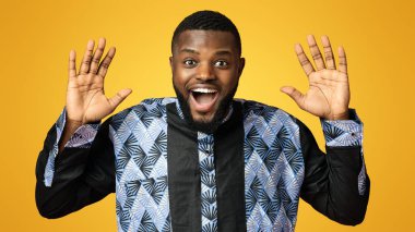 İnanamıyordum. Şaşırmış, elleri havada pembe arka planda kameraya bakan, geleneksel Afrika kostümü giymiş siyahi bir adam. Duygusal Afrikalı Amerikalı genç adam stüdyoda poz veriyor.