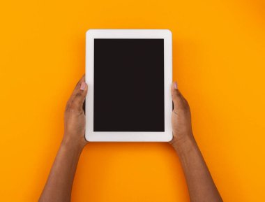 Siyah ekranlı modern dijital tablet. Kadın eli turuncu arka planda, boş alan.