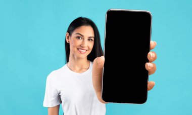 Mobil Uygulama Model Model. Siyah beyaz ekranlı büyük akıllı telefonu gösteren güzel genç bir kadın tasarımın ya da reklamın için bedava fotokopi alanı gösteren gülümseyen bir kadın mavi arka planda poz veriyor.