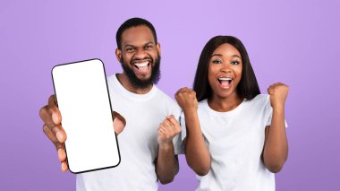 Büyük Galibiyet Kavramı. Heyecanlı genç Afrikalı Amerikalı çift tezahürat yapıyor ve ellerini kaldırıyor, zaferi kutluyorlar. Duygusal mutlu erkek ve kadın poz veriyor ve sıkılmış yumruklar, mavi stüdyo arka planı, afiş