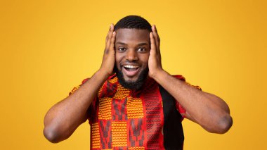 Parlak geleneksel tişörtlü süper mutlu zenci kafasına dokunuyor, şansına inanamıyor, sarı arka plan