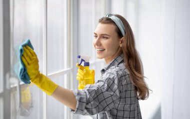 Lastik eldivenli güzel bir bayanın portresi. Evde deterjanıyla pencereyi temizliyor. Sevgili milenyum ev hanımı evini düzenli tutuyor, ev işlerini mutlu bir şekilde yapıyor, ev işlerinden zevk alıyor.