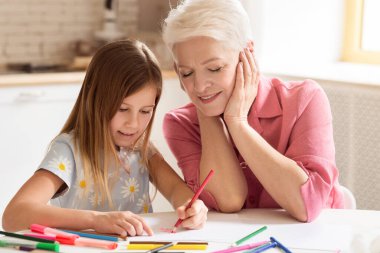Yaratıcılık geliştiriyor. Büyükbaba ve torun mutfakta renkli kalemlerle çizim yapıyorlar.