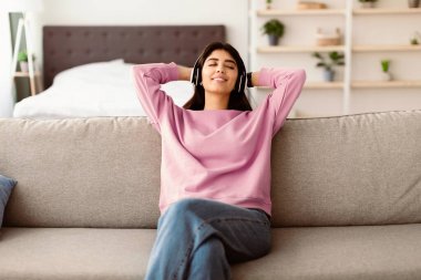 Dinlen ve rahatla kavramı. Sakin genç bir kadının portresi kanepede uzanıyor, müzik dinliyor, sesli kitap dinliyor, podcast yapıyor, uyku için meditasyonun keyfini çıkarıyor ve kablosuz kulaklıklarda huzurlu bir zihin, kopyalama alanı.