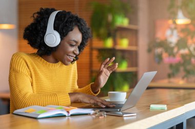 Afro girl in headset using laptop at cafe, having skype conference, free space