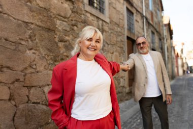 Neşeli bir çift, güzel bir kaldırım taşı caddesinde el ele yürür. Kırmızı elbiseli kadın, etraflarındaki tarihi mimariyi keşfederken neşe saçar..