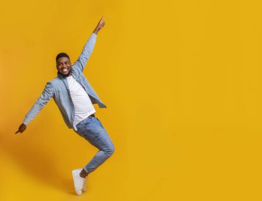 Stüdyoda sarı arka planda parmak uçlarında poz veren komik Afrikalı Amerikalı adam.