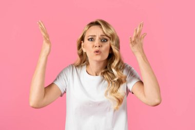 Genç bir kadın parlak pembe bir arka planda duruyor, hayal kırıklığına uğramış ve kafası karışmış görünüyor. İnançsızlık içinde ellerini kaldırıyor, beklenmedik bir şeye tepki verirken dalgalı saçları yüzünü çerçeveliyor..