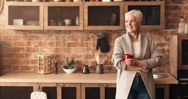 Kahve molası. Sakin yaşlı bayan mutfakta duruyor, kahve içiyor ve boş alana bakıyor, panorama