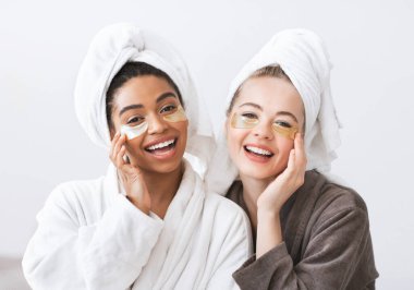 Neşeli genç çok ırklı kadınlar göz bandı takıyor, evde yüz bakımı yaptırıyorlar.