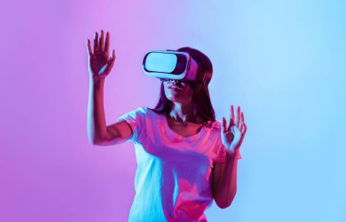 Modern cihaz. Sanal gözlüklü Asyalı kadın elini kaldırdı, neon ışıklı, stüdyo fotoğrafı.