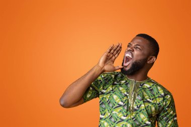 Dikkat! Yeşil elbiseli duygusal siyah adam sarı arkaplan ve panorama üzerinden kopyalama alanına doğru bağırıyor.