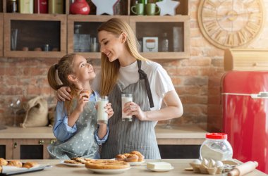 Güzel anne ve kız mutfakta birlikte vakit geçiriyorlar, kek yiyip süt içiyorlar, fotokopi çekiyorlar.