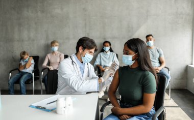 Afrika kökenli Amerikalı genç bir kadın COVID-19 aşısı yaptırıyor. Aşıların yapıldığı sitede. Uluslararası bir grup hasta hastanede koronavirüs salgını sırasında aşı olmayı bekliyor.