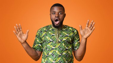 Geleneksel kostümlü, ağzı açık, elleri açık, sarı stüdyo geçmişi olan Afrikalı bir adam şaşırdı.