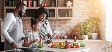 Modern teknolojiler ve yemek pişirme. Siyah kadın, adam ve onların sevimli kızı tablet tarifi okuma, mutfakta yemek, kopya alanı