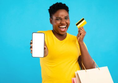 Mobil Alışveriş Uygulaması. Heyecanlı Siyah Kadın Akıllı Telefon Boş Ekran Kredi Kartı Gösteriyor Mavi Stüdyo Arkaplanının Üzerinde Duruyor. Kadın Alışverişci Uygulama ve Telefon Bankasını Öneriyor. Model
