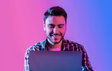 İşyerinde serbest çalışan biri. Neon Stüdyoda dizüstü bilgisayarı olan gülümseyen genç adam.