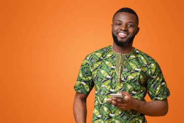 Otantik Afrika kostümlü gülümseyen siyah adam cep telefonu, sarı arka plan, kopyalama alanı kullanıyor.