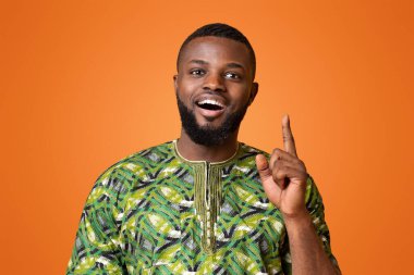 Geleneksel giyinmiş siyahi bir adamın harika bir fikri var. Parmağını kaldırıp, sarı stüdyonun arka planına bakıyor.