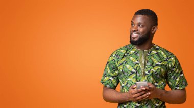 Cep telefonlu mutlu siyah adam fotokopi alanına bakıyor, sarı arka plan, panorama