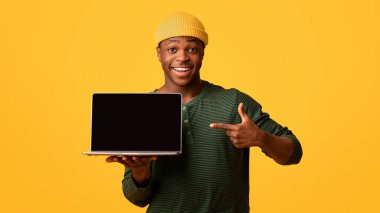 Güzel web sitesi. Siyah boş ekranlı dizüstü bilgisayarı işaret eden neşeli Afrikalı Amerikalı adam tasarımın için bedava kopyalama alanı sunuyor, sarı arka planda izole edilmiş,