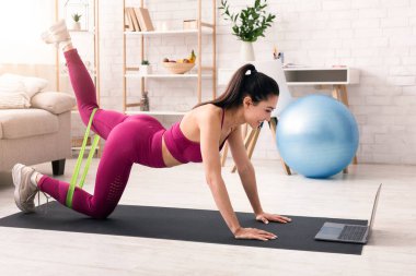 Evde kal, formda kal. Evde dizüstü bilgisayarın önünde elastik bantla çalışan mutlu kız.