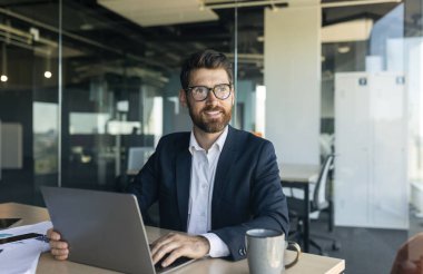 Mature male entrepreneur using laptop and thinking, looking aside while sitting at workplace in office, free space. Successful entrepreneurship career concept