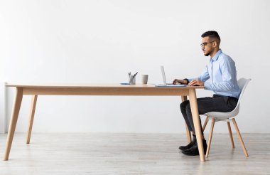 Modern ofiste dizüstü bilgisayarda çalışan odaklanmış Orta Doğulu erkek müdürün profil görüntüsü, masada oturan ve bilgisayar kullanan ciddi bir adam, ekrandaki Webinar 'a bakıyor.