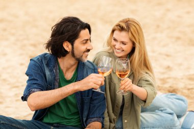 Bir adam ve bir kadın kumda oturmuş kadehlerini kaldırırken gülümsüyorlar. Sıcak günbatımı, birlikte geçirdikleri zamanın keyfini çıkarırken romantik bir parıltı salıyor..