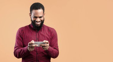 Online Mobil Oyunlar. Gülümseyen siyah adam cep telefonu tutuyor ve oynuyor, sarı duvarın üzerinden izole edilmiş, kopyalanmış.