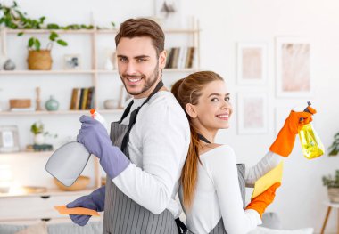Evde büyük temizlik var. Önlüklü ve lastik eldivenli gülümseyen karı-koca modern oturma odasının iç kısımlarına sprey sıkmışlar.