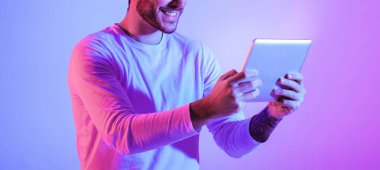 Elinde tablet, kesilmiş, panorama olan neonlu mutlu bir adam.