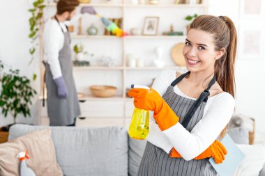Birlikte temizlik yapıyoruz. Spreyle gülümseyen genç kadın, oturma odasındaki meşgul kocayı işaret ediyor, boş yer.