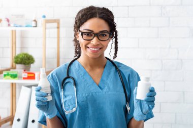 Gülümseyen Afro-Amerikan veteriner doktor hayvan kliniğinde farklı ilaçlar tutuyor.