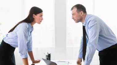 İş yerinde anlaşmazlık. İş adamı ve iş kadını, modern ofiste tartışırken birbirlerine dik dik bakıyorlar..