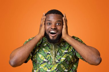 Geleneksel Afrikalı kıyafetleri içindeki hayret verici zenci adam sarı arka planda kafasına dokunuyor.